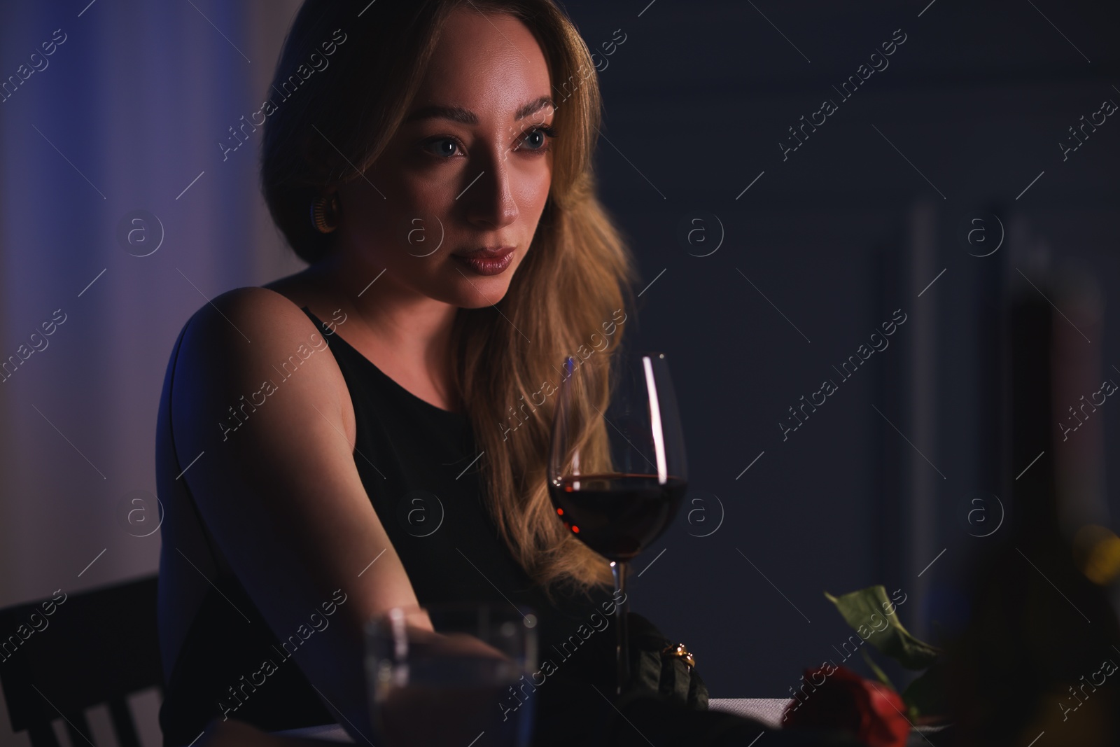 Photo of Elegant young woman with glass of wine at table indoors in evening