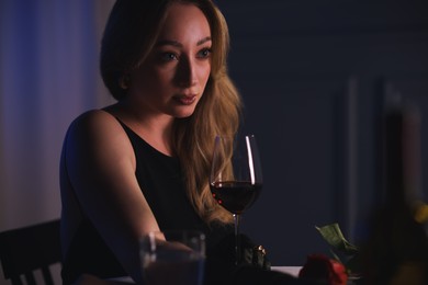 Photo of Elegant young woman with glass of wine at table indoors in evening