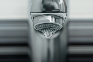 Photo of Water drop falling down from tap on blurred background, closeup