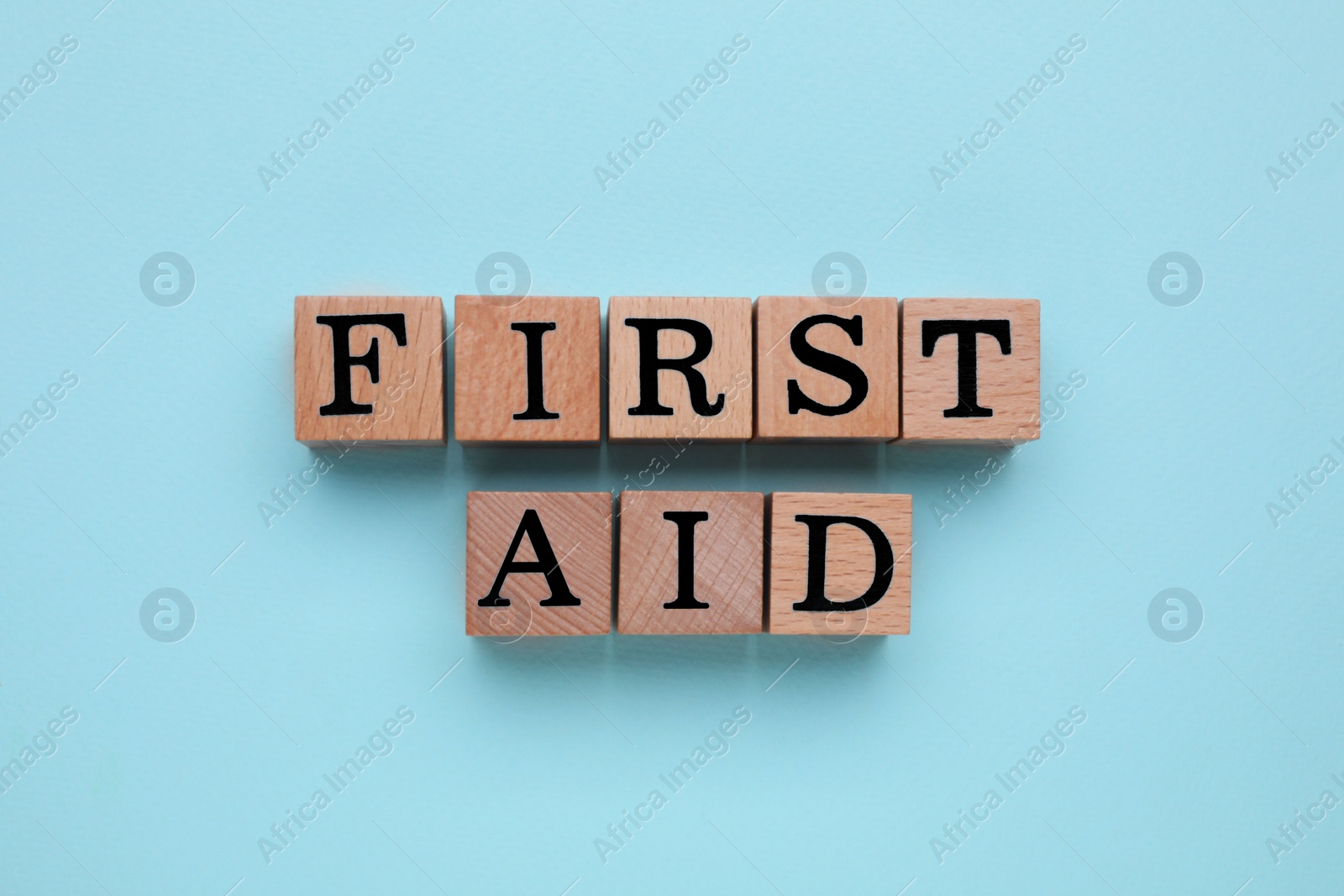 Photo of Words First Aid made of wooden cubes on light blue background, top view