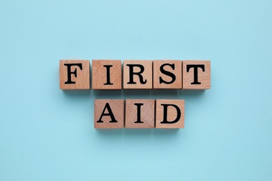 Photo of Words First Aid made of wooden cubes on light blue background, top view