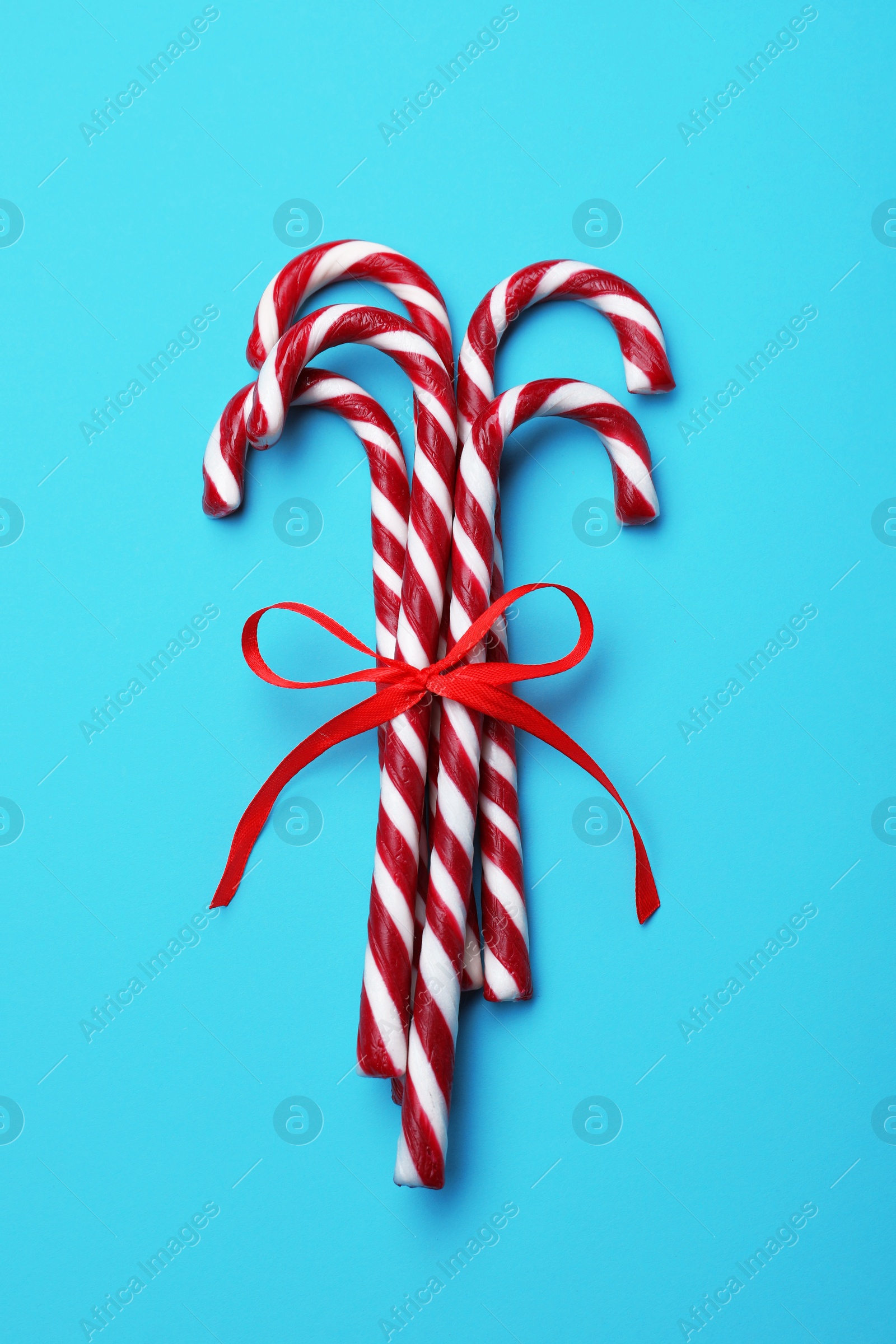 Photo of Sweet Christmas candy canes with red bow on light blue background, top view