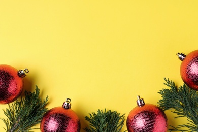 Beautiful red Christmas balls and fir branches on yellow background, flat lay. Space for text