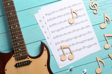 Guitar neck and sheets with music notes on color wooden background, flat lay