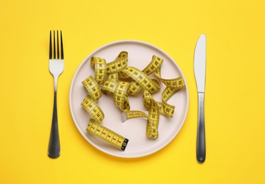Photo of Measuring tape, fork and knife on yellow background, flat lay. Weight loss concept