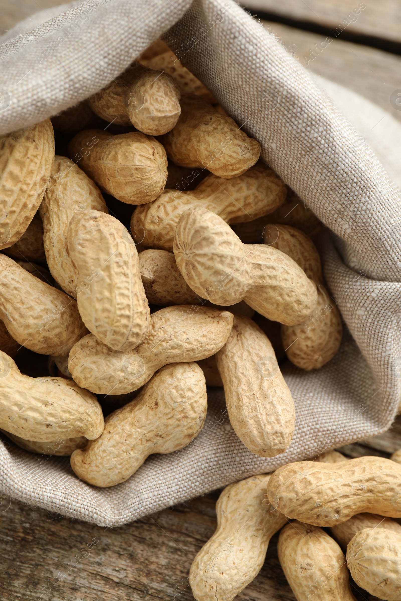 Photo of Fresh unpeeled peanuts in sack on wooden table