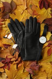 Photo of Stylish black leather gloves, glasses and wristwatch on dry leaves, flat lay