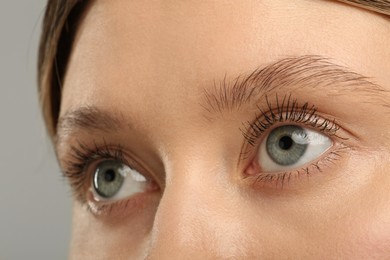 Woman with long eyelashes after mascara applying against grey background, closeup