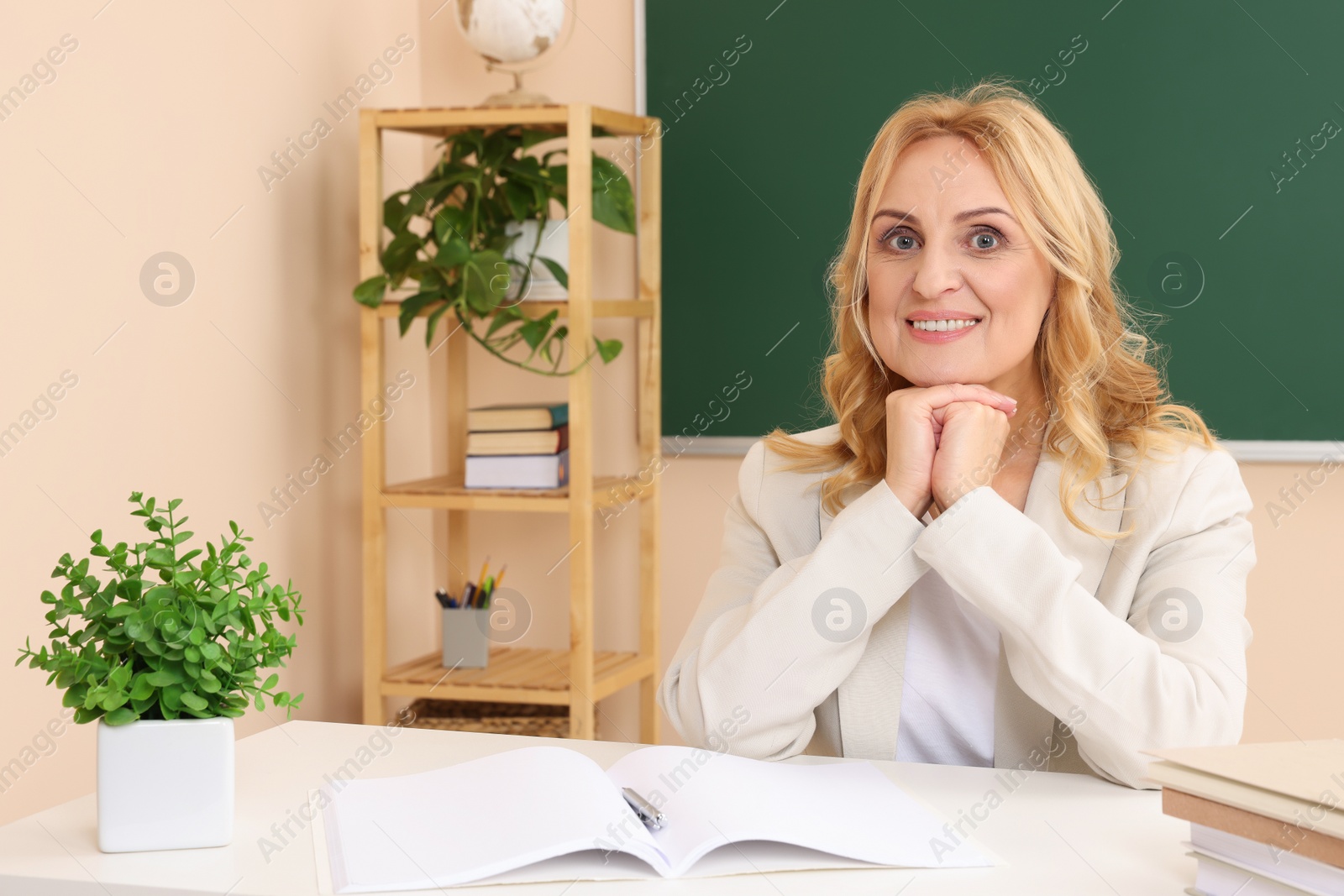 Photo of Happy professor with books sitting at desk in classroom