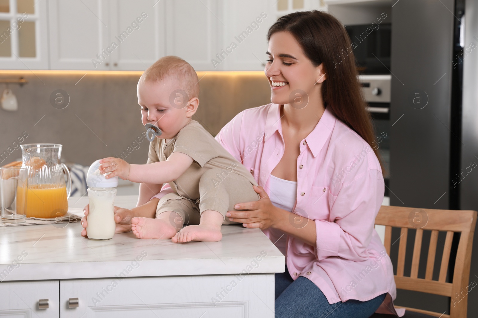 Photo of Happy young woman with her cute little baby in kitchen