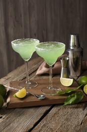 Photo of Delicious Margarita cocktail in glasses, limes and bartender equipment on wooden table