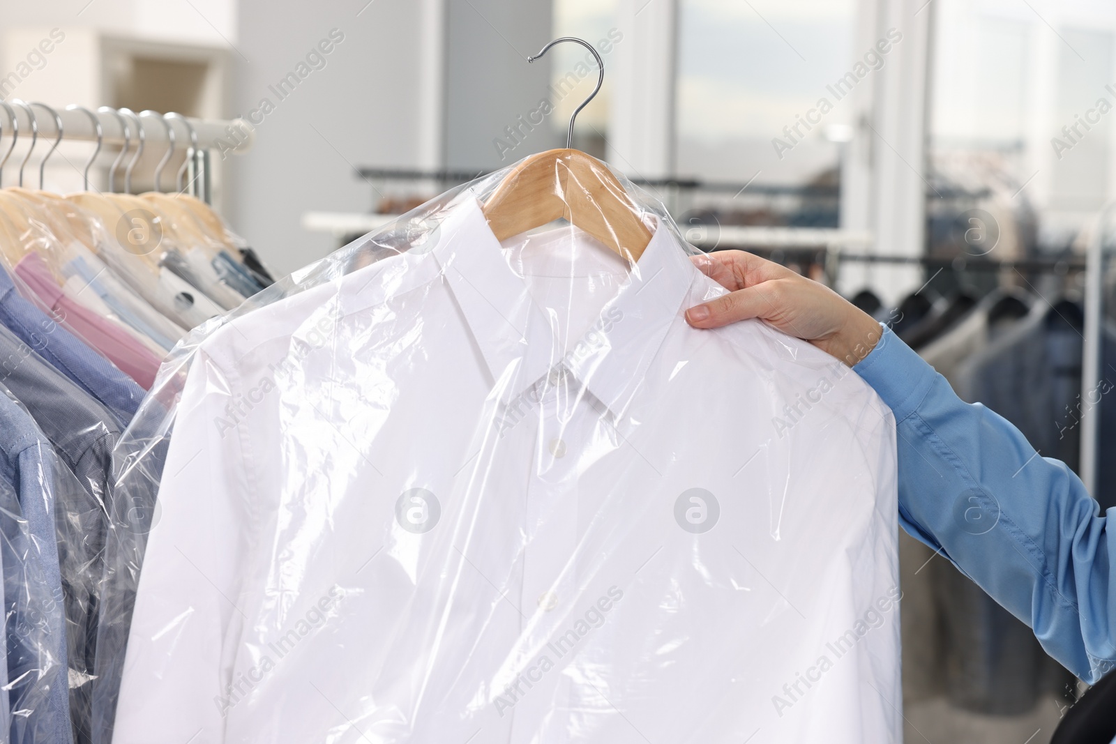 Photo of Dry-cleaning service. Woman holding shirt in plastic bag indoors, closeup