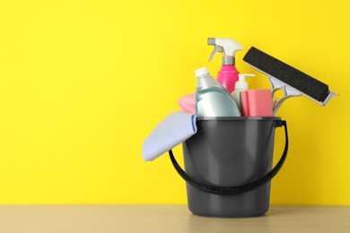 Photo of Bucket with different cleaning supplies on wooden floor near yellow wall. Space for text