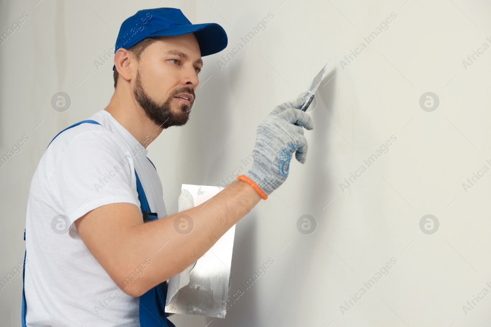 Photo of Professional worker plastering wall with putty knives indoors