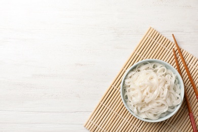 Photo of Bowl with rice noodles on wooden table, top view. Space for text
