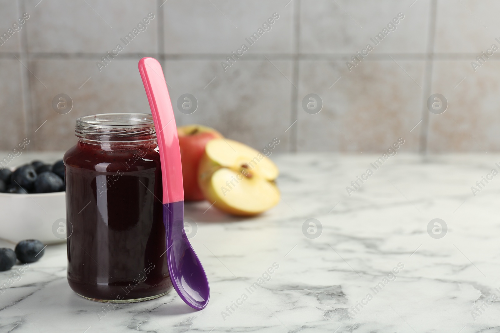 Photo of Tasty baby food in jar and spoon on white marble table. Space for text