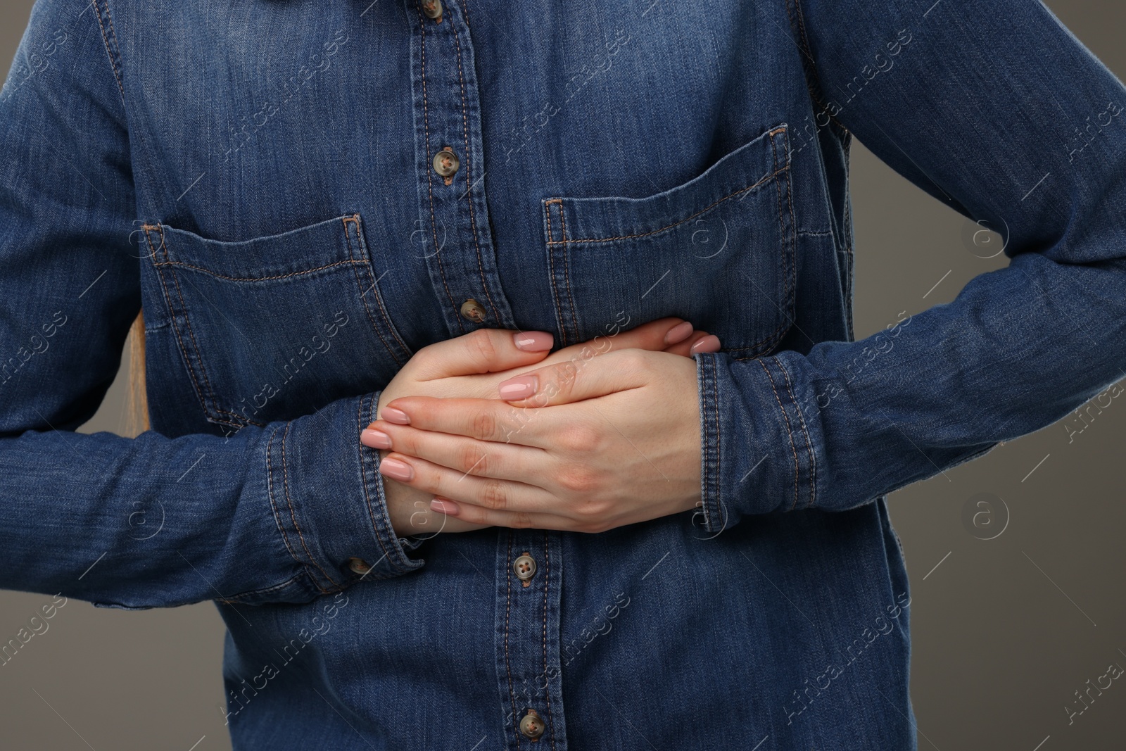 Photo of Woman suffering from stomach pain on grey background, closeup