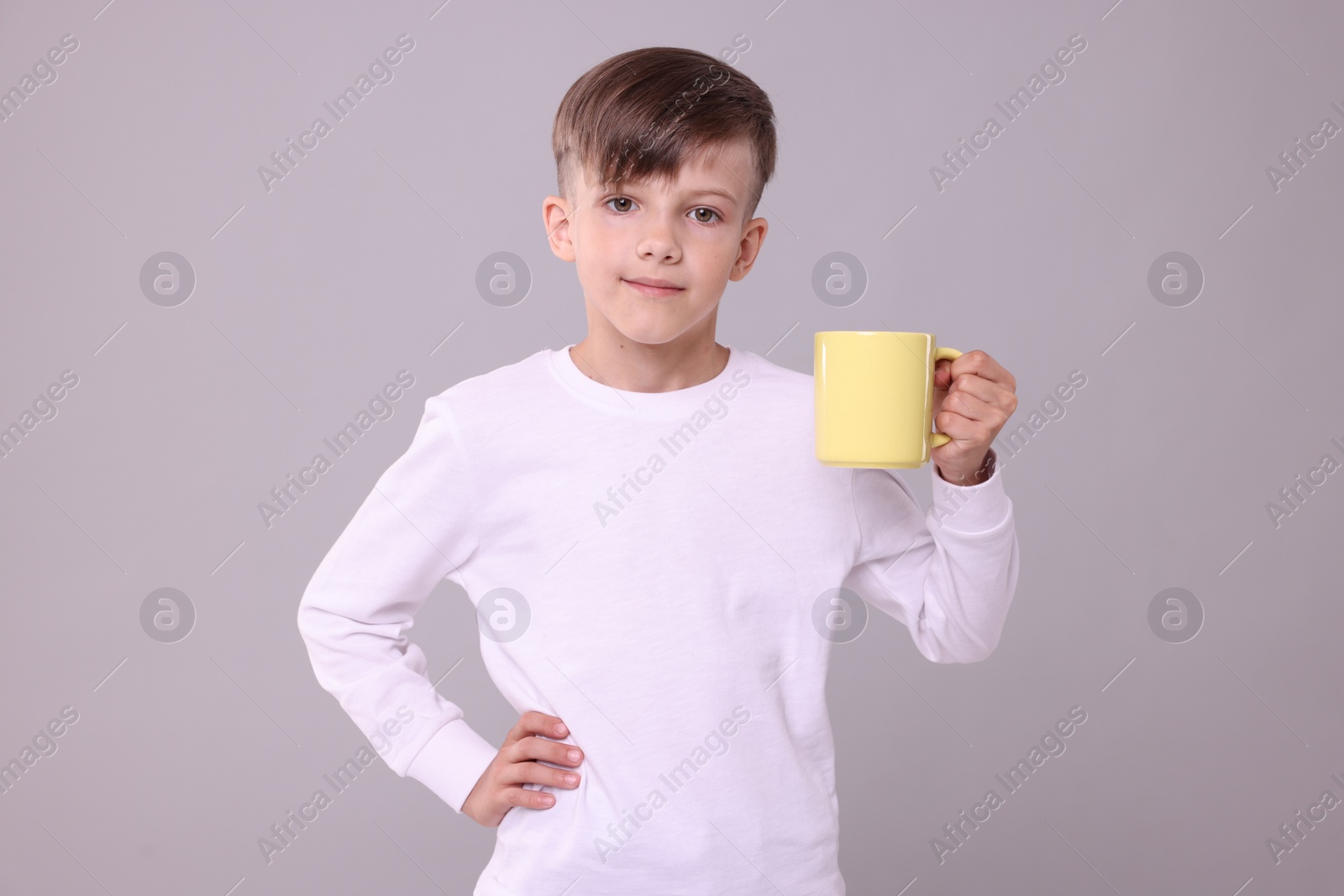 Photo of Cute boy with yellow ceramic mug on light grey background