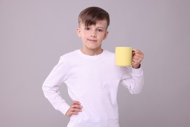 Cute boy with yellow ceramic mug on light grey background