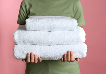 Woman holding stack of fresh towels on pink background, closeup