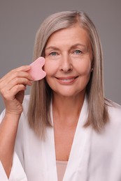 Woman massaging her face with rose quartz gua sha tool on grey background