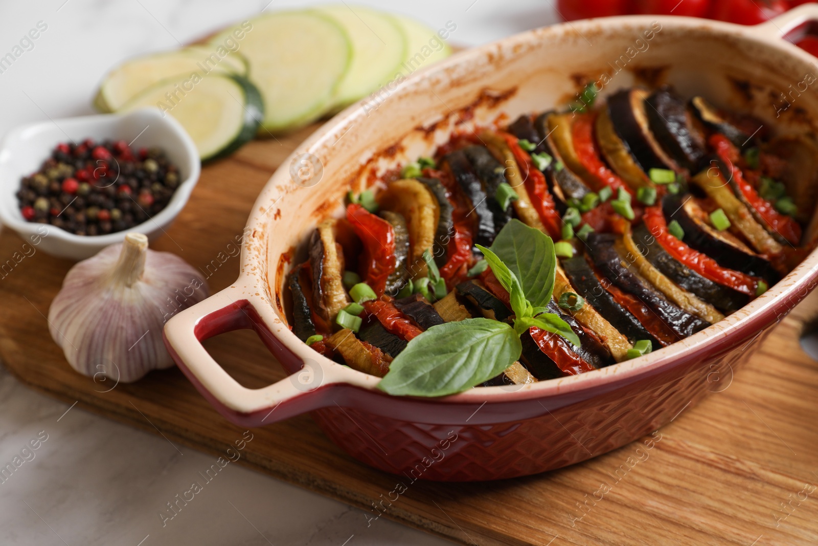 Photo of Delicious ratatouille in dish and ingredients on table, closeup