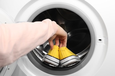 Photo of Woman putting stylish sneakers into washing machine, closeup