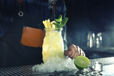 Photo of Barman with tropical cocktail at counter in pub, closeup. Space for text