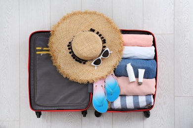 Open suitcase with female clothing and accessories on wooden background