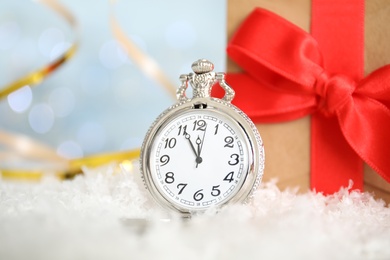 Photo of Pocket watch and gift on snow against blurred lights. New Year countdown