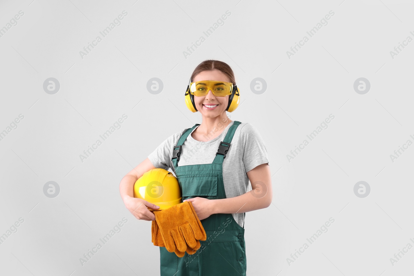 Photo of Female industrial worker in uniform on light background. Safety equipment