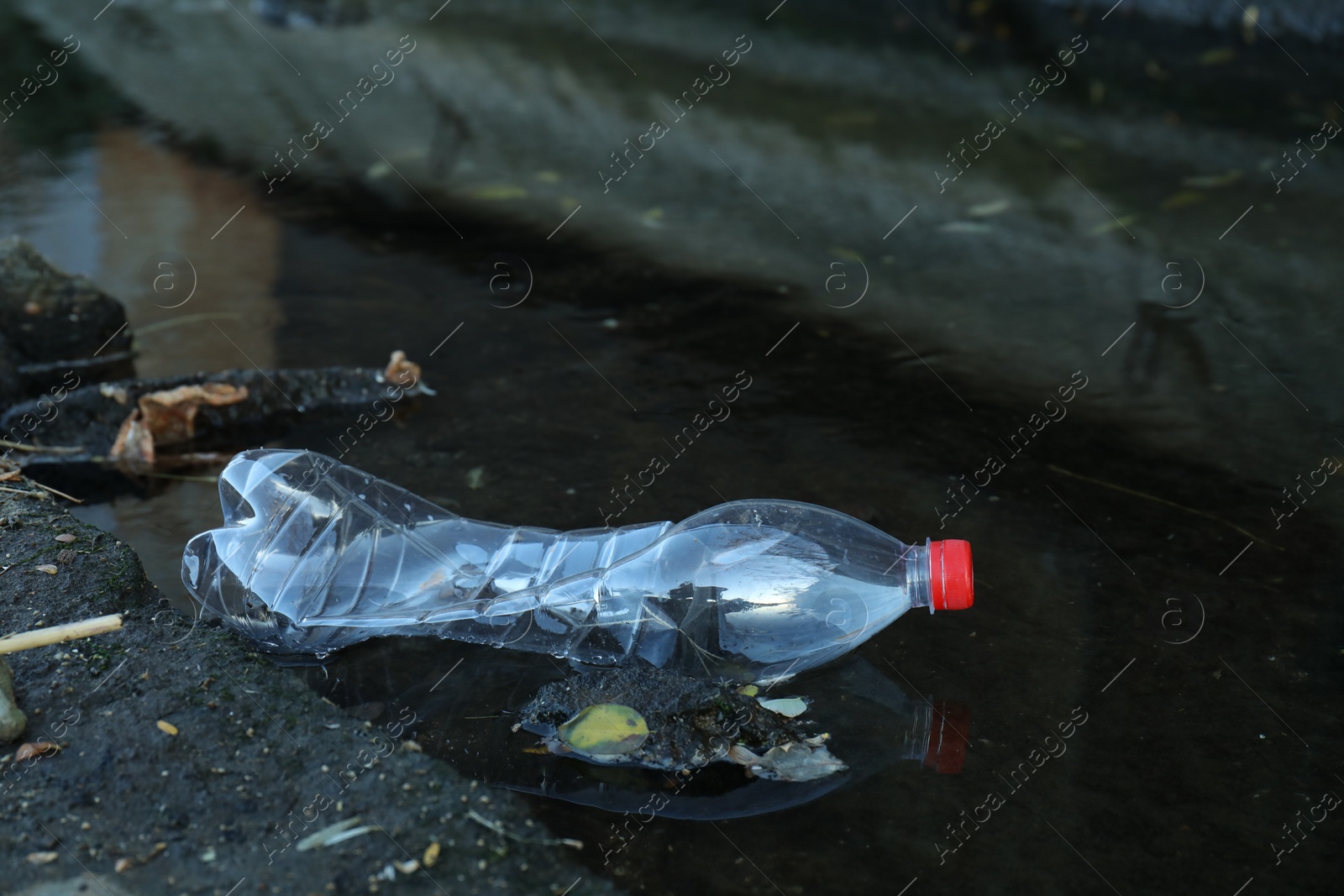 Photo of Used plastic bottle near water outdoors. Environment pollution