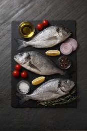 Photo of Fresh raw dorado fish, lemon wedges, spices and tomatoes on black table, flat lay