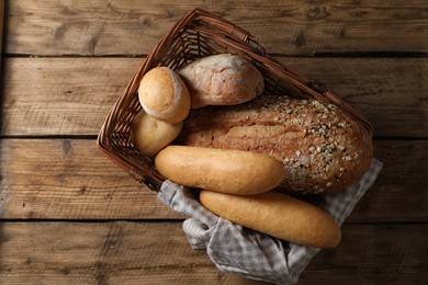 Wicker basket with different types of bread on wooden table, top view