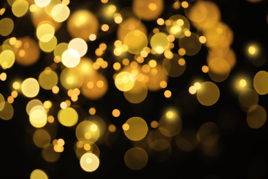 Blurred view of gold lights on black background, bokeh effect