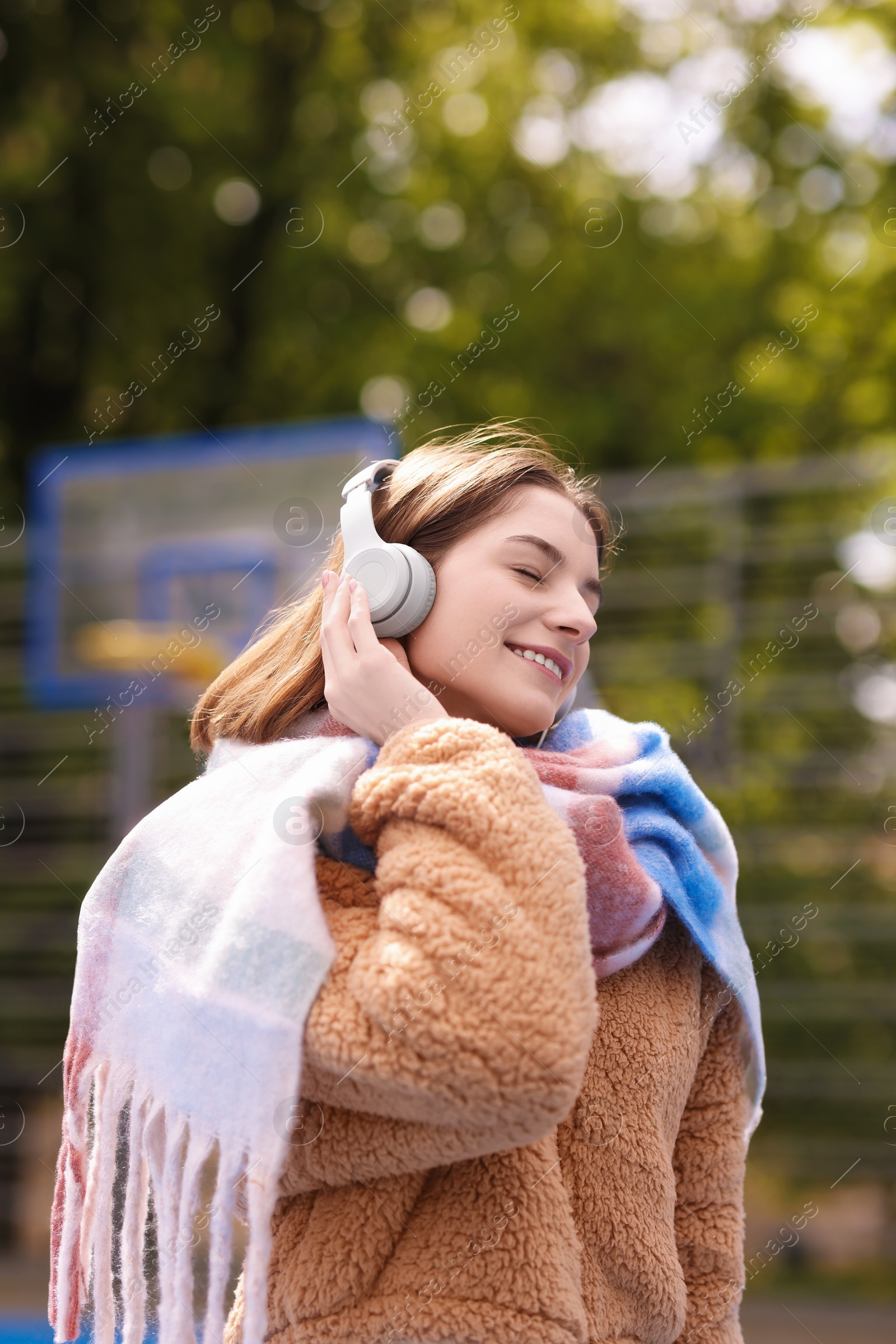 Photo of Beautiful woman in warm scarf listening to music outdoors