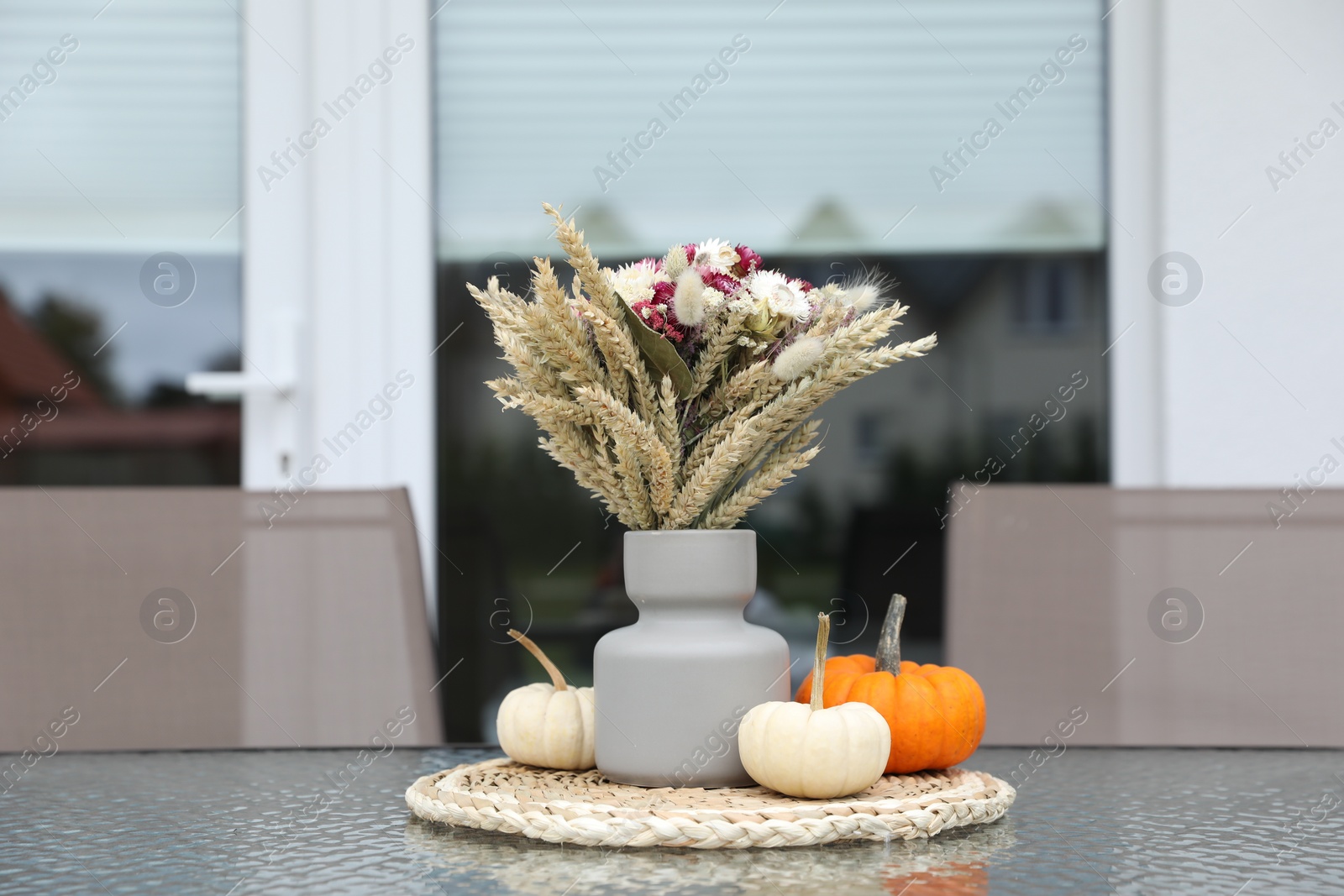 Photo of Beautiful bouquet of dry flowers and small pumpkins on glass table outdoors