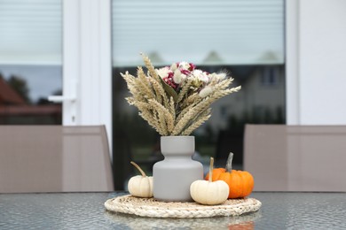 Photo of Beautiful bouquet of dry flowers and small pumpkins on glass table outdoors