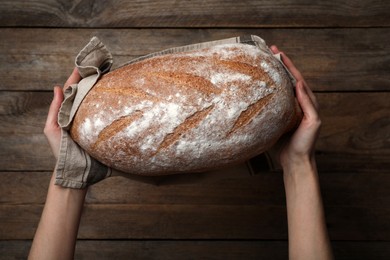 Photo of Woman holding loaf of tasty wheat sodawater bread at wooden table, top view