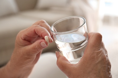 Photo of Senior woman with glass of water taking pill at home, closeup