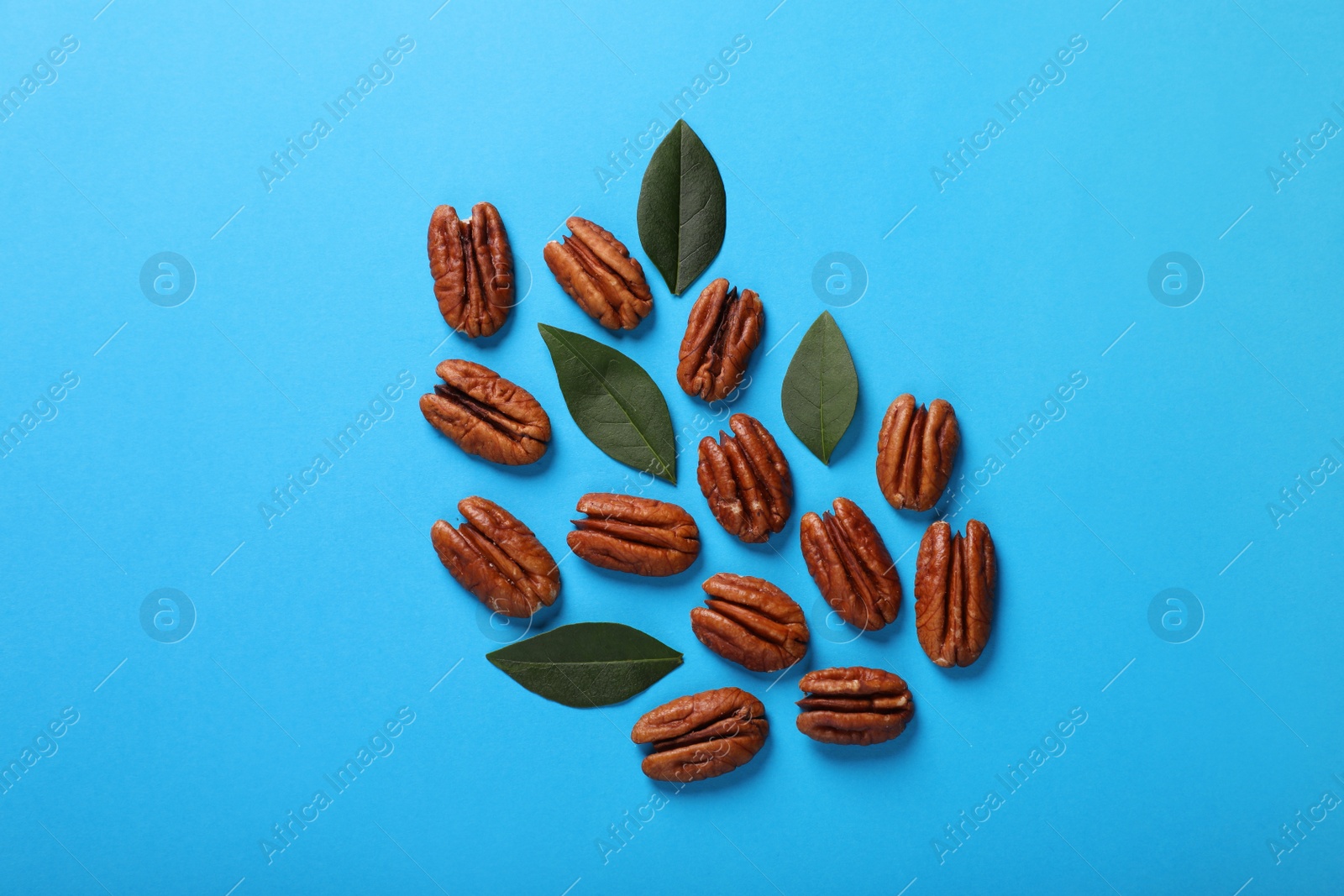 Photo of Delicious pecan nuts and green leaves on light blue background, flat lay