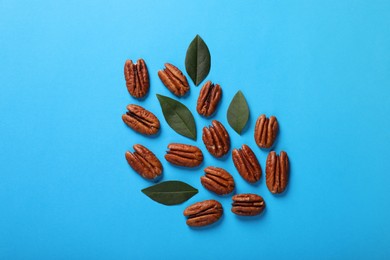 Delicious pecan nuts and green leaves on light blue background, flat lay