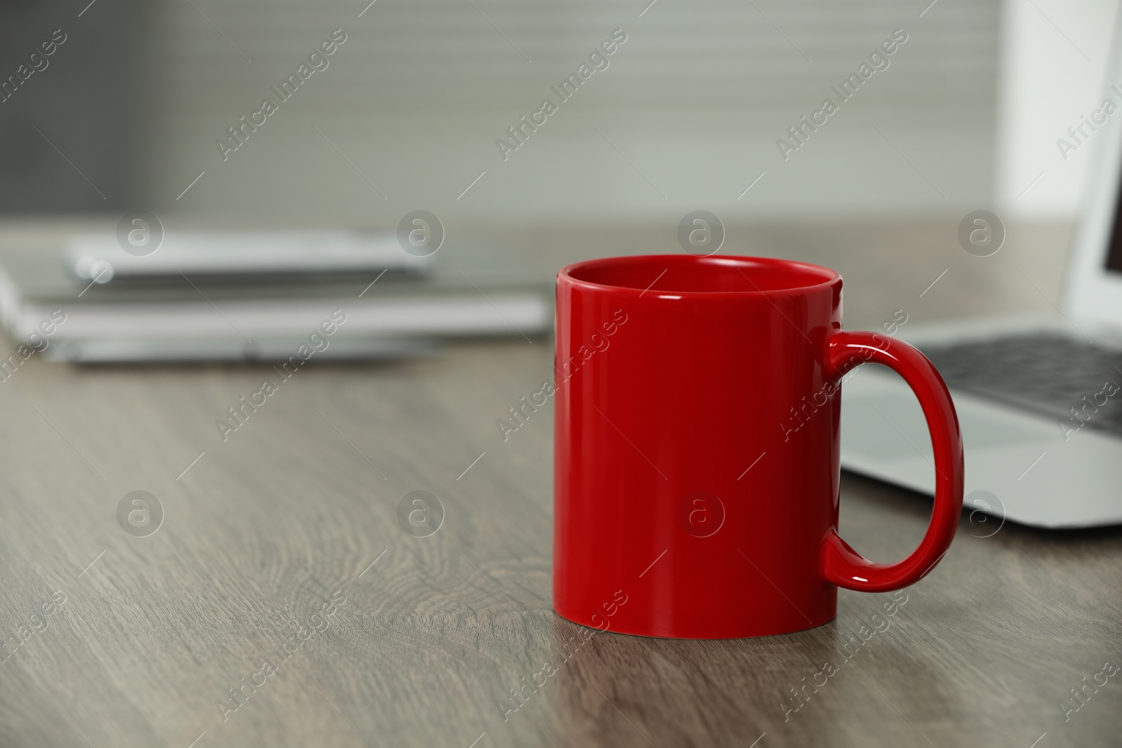 Photo of Red ceramic mug on wooden table at workplace. Mockup for design