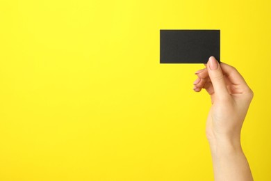 Woman with blank black business card on yellow background, closeup. Mockup for design