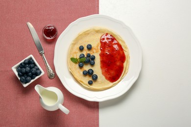 Photo of Stack of delicious crepes with fresh berries and jam on white table, flat lay. Space for text