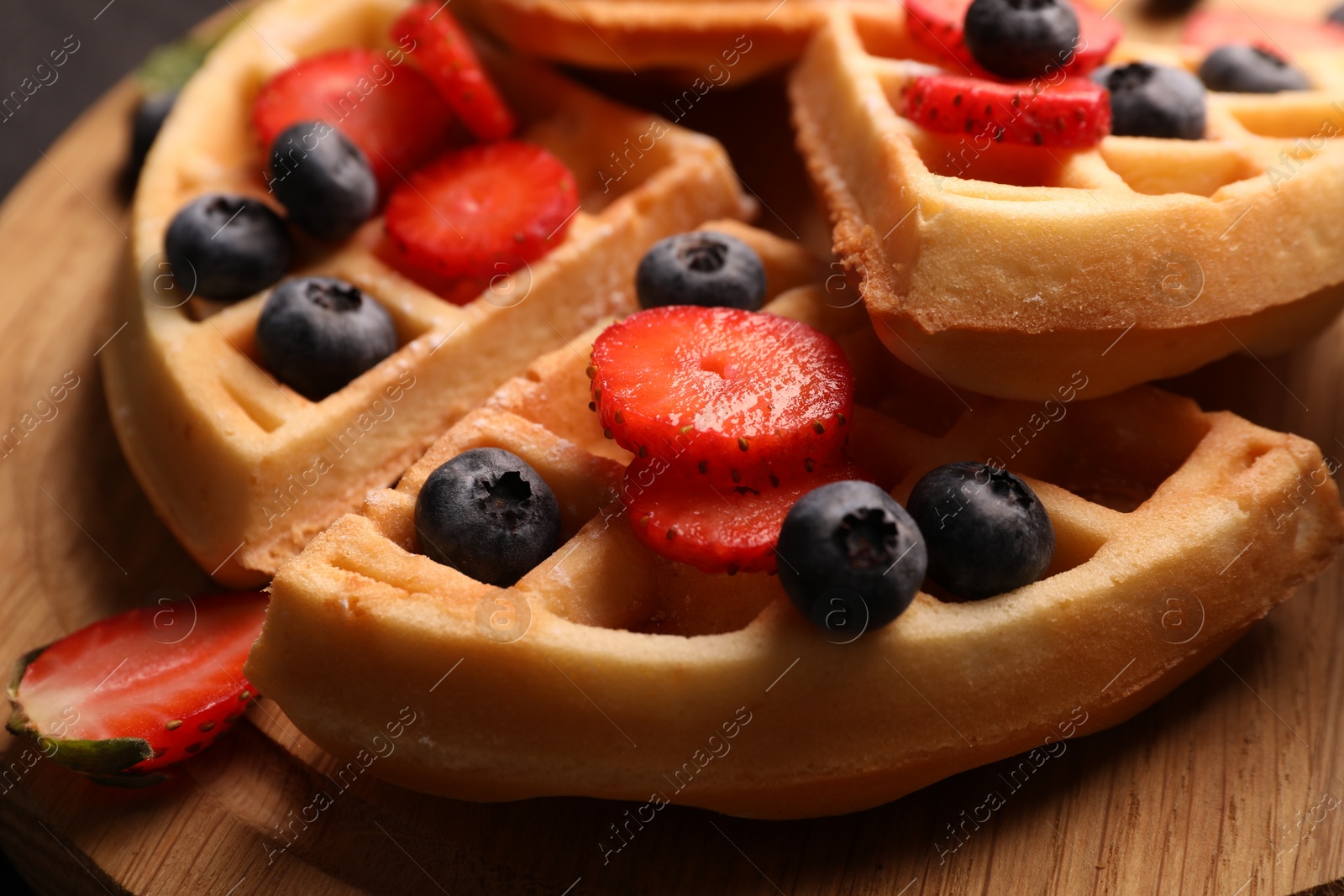 Photo of Tasty Belgian waffles with fresh berries on wooden board, closeup