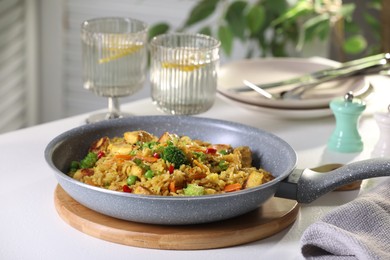 Tasty rice with meat and vegetables in frying pan on white table indoors