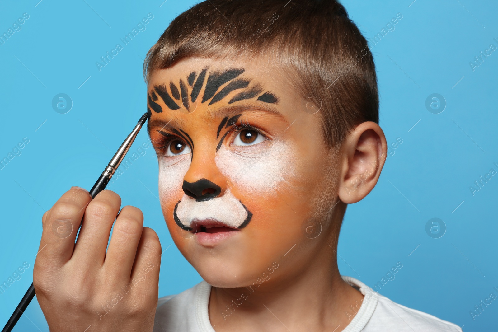 Photo of Artist painting face of little boy on blue background