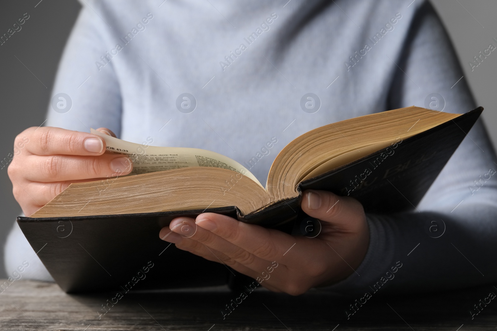 Photo of Woman reading Bible at wooden table, closeup