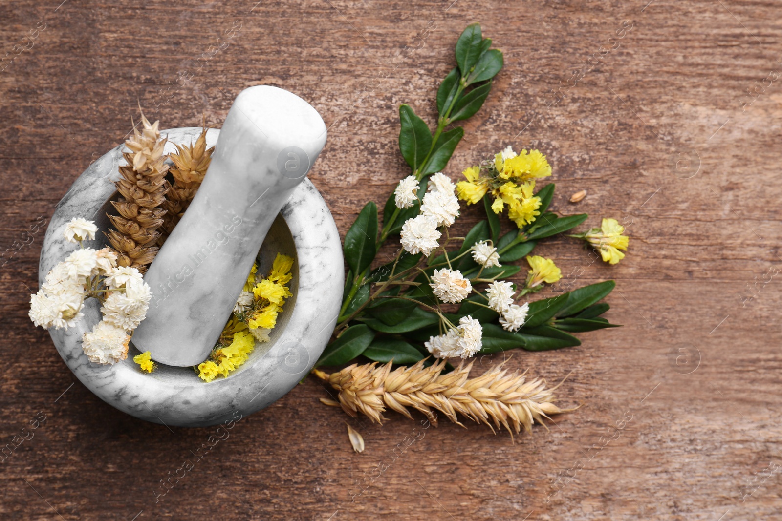 Photo of Mortar with pestle, dry flowers and ears of wheat on wooden table, flat lay